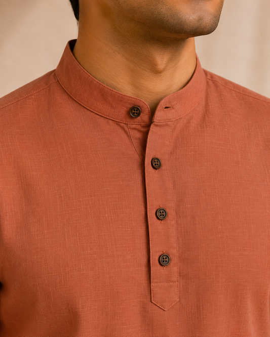 Close-up of a man wearing a brick red linen kurta with a mandarin collar and dark buttons.