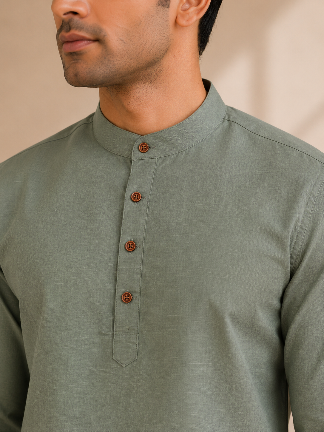 A close-up of a man wearing an olive green kurta with a mandarin collar and brown buttons.