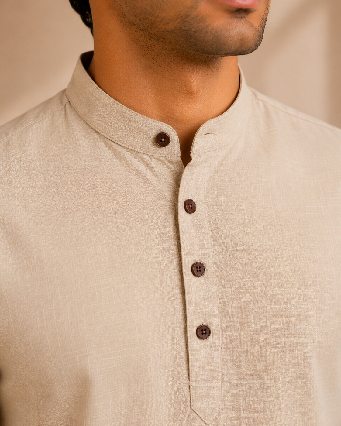 Close-up of a man wearing a blush beige linen kurta with a mandarin collar and dark brown buttons.